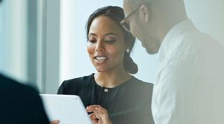 Two smiling colleagues standing together looking at an iPad